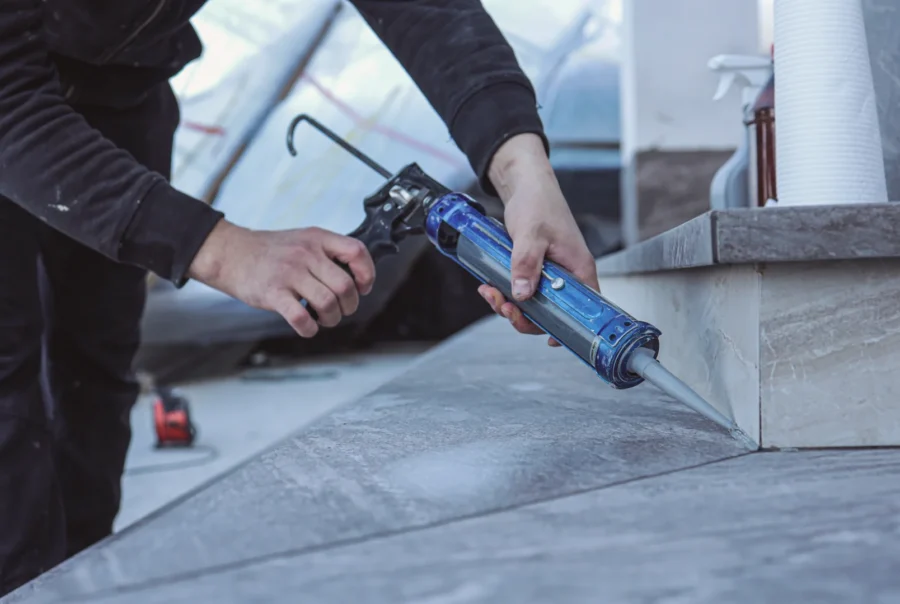 contractor using a caulking gun to apply weatherproof coating along the seams of the roof