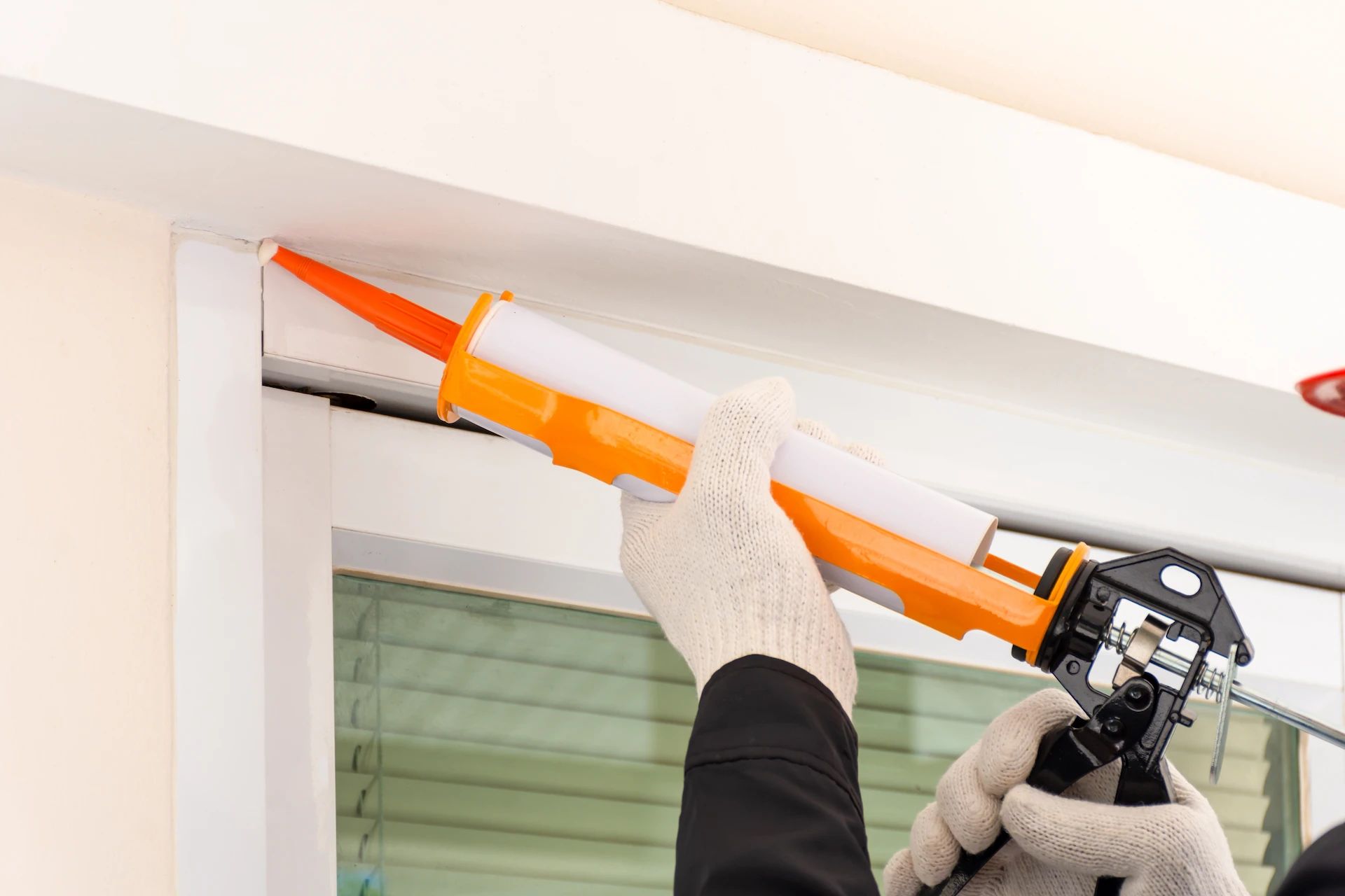 contractor holding a caulking gun and injecting caulking into a window frame